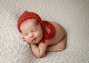 Newborn posed in red bonnet