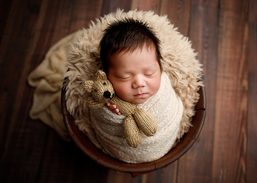 Newborn Photographer Sleeping newborn baby wrapped in cream and posed with a teddy bear