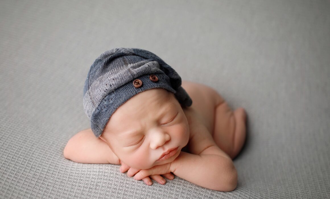 baby boy posed for newborn photoshoot on grey blanket